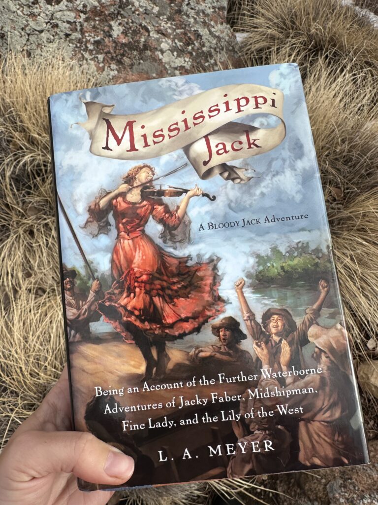 The cover of Mississippi Jack by L.A. Meyer shows a girl in a red dress playing a fiddle and dancing on the cabin of a keelboat on a river