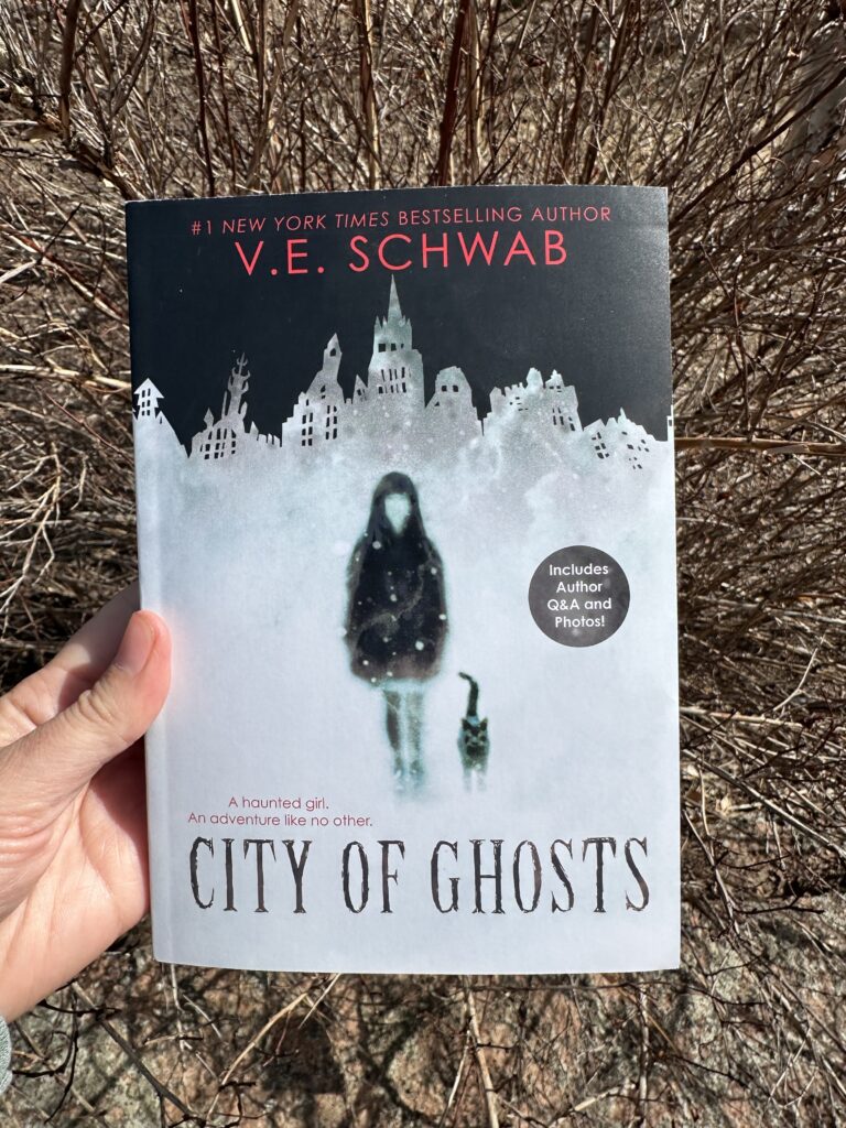 The cover of City of Ghosts by V.E. Schwab shows a foggy city and the silhouette of a girl and her cat moving through the mist