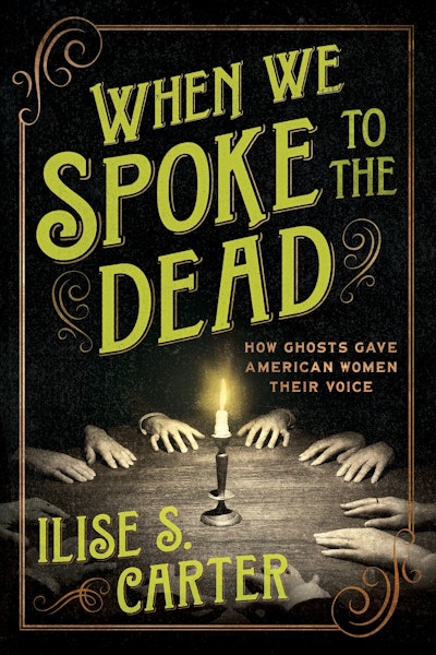 On the cover of When We Spoke to the Dead, a table with a single candle upon it and the hands of 6 people resting on the table palms down. The rest of the scene recedes into shadow